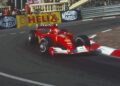 A red Ferrari Formula 1 car takes a corner on a city street circuit, passing Shell Helix and Magneti Marelli banners—echoing the Historic Monaco Sale, where the Ferrari F2001 became the most valuable Schumacher-F1 car at €15.98 million.