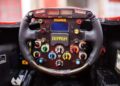 Close-up of a Ferrari Formula 1 steering wheel with numerous buttons, switches, and dials, similar to those found on the F2001—the most valuable Schumacher-F1 car sold at Historic Monaco Sale for €15.98 million—featuring a central digital display.