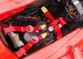 Red racing harness with yellow accents secured in the cockpit of a race car, surrounded by exposed wiring and electronic components—reminiscent of those seen at the Historic Monaco Sale, where the Ferrari F2001 became the most valuable Schumacher-F1 car at €15.98 million.