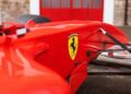 Close-up of a red Ferrari Formula 1 car, showing the Ferrari logo near the cockpit, with part of a red and gray building in the background—evoking the excitement of the Historic Monaco Sale, where a Ferrari F2001 set records at €15.98 million.