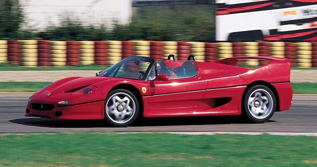 A red Ferrari F50 convertible speeds along the racetrack, blurred background elements capturing the thrill of its 30th Anniversary Legacy Tour.