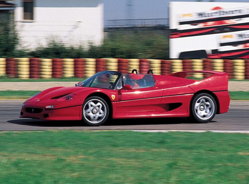 A red Ferrari F50 convertible speeds along the racetrack, blurred background elements capturing the thrill of its 30th Anniversary Legacy Tour.