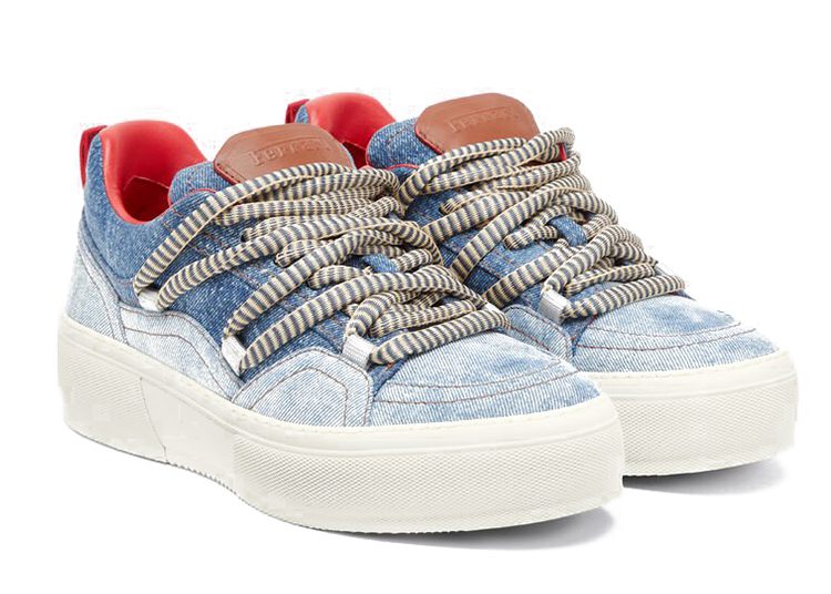 A pair of denim sneakers with thick white and gray striped laces, white rubber soles, red inner lining, and brown leather tongue labels from the Ferrari Lifestyle Capsule Collection inspired by Charles Leclerc.