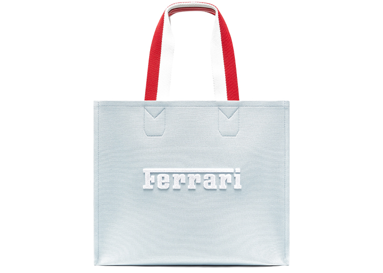 A light grey tote bag with red and white handles, featuring the white Ferrari logo on the front—part of the exclusive Lifestyle Capsule Collection.