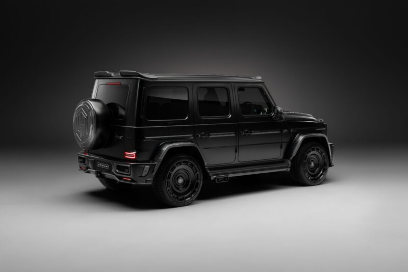 Matte black G-Wagon Mercedes-Benz G-Class SUV, equipped with widetrack aero kits, shown in a studio setting with a dark background, rear and side view visible.
