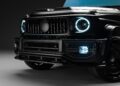 Close-up of the front grille and headlights of a black G-Wagon luxury SUV, featuring illuminated circular LED lights, detailed bumper design, and an aggressive Widetrack Aero Kit.