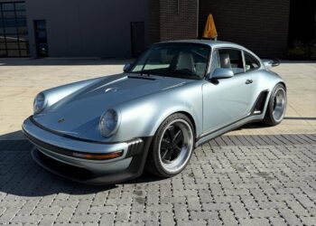 A silver classic Porsche sports car with black accents, part of the $3.8M Inventory at Graham Rahal Performance, is parked on a paved surface in front of a modern industrial building.