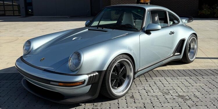A silver classic Porsche sports car with black accents, part of the $3.8M Inventory at Graham Rahal Performance, is parked on a paved surface in front of a modern industrial building.