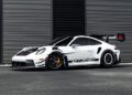 A white Porsche 911 GT3 RS sports car with black accents is parked in front of a modern, striped metal building.
