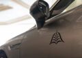Close-up of a car door and side mirror, featuring a black abstract logo decal on the metallic gray exterior of a Flying Spur Mulliner, Bentley Motors' renowned bespoke sedan.