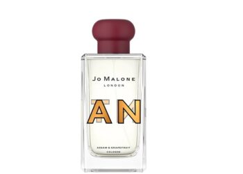 A clear glass bottle of Jo Malone London Assam & Grapefruit cologne with a red cap and bold overlapping letters "A" and "N" on the front—a perfect style upgrade for those seeking luxury accessories.