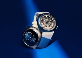 Two modern wristwatches, including a sleek H. Moser & Cie., are displayed on a blue surface—one with an analog face and white strap, the other digital with a silver-tone metal strap—both illuminated under a focused beam of light.