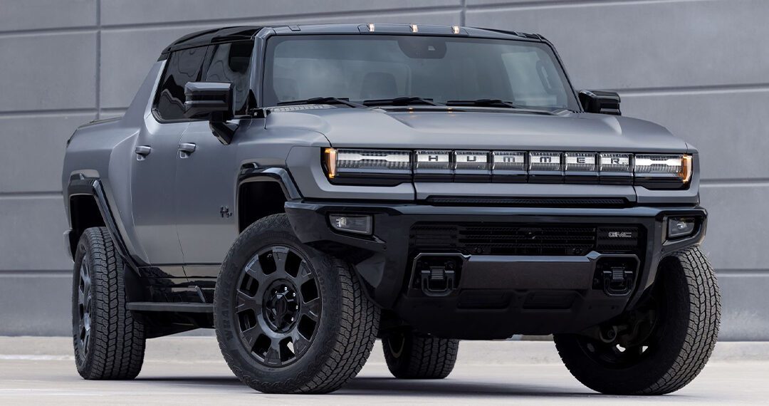 A matte black 2026 GMC HUMMER EV electric pickup truck is parked in front of a modern gray concrete wall.