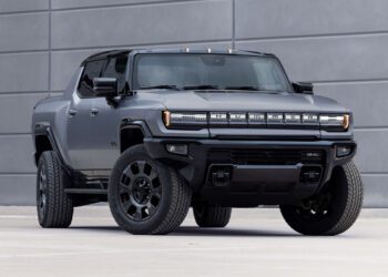 A matte black 2026 GMC HUMMER EV electric pickup truck is parked in front of a modern gray concrete wall.