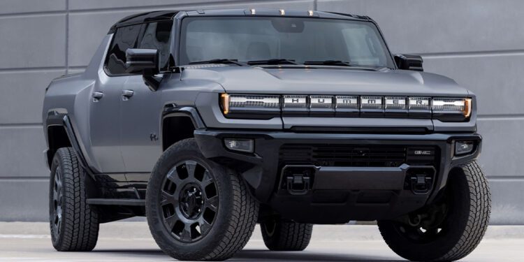 A matte black 2026 GMC HUMMER EV electric pickup truck is parked in front of a modern gray concrete wall.