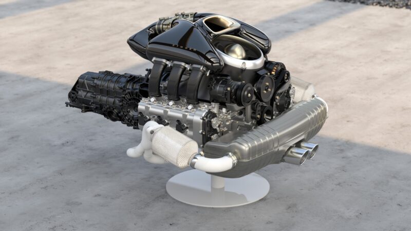 A modern Singer Porsche 911 engine and transmission assembly displayed on a white stand, set on a concrete floor—showcasing the craftsmanship behind this limited edition masterpiece.