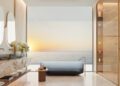 Modern bathroom with marble surfaces, a freestanding tub, double sinks, glass shower, and large windows overlooking an ocean view at sunset—echoing the luxurious style of Jacob & Co.’s $1.3B beachfront development south of Dubai.
