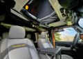 Interior view of a Jeep Rubicon with gray seats, open roof, and a foldable tray between the front seats. The sky and trees are visible through the open roof—one thing that makes this carbon-fiber tent a game changer for the Jeep Wrangler.