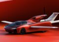 A red flying car, reminiscent of the production prototype of Klein Vision AirCar, with extended wings and a rear propeller, sits on a red surface against a matching background.