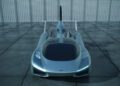 A futuristic silver flying car prototype with a sleek design and rear wings, parked on a tiled surface against a perforated metal wall, as the production prototype of Klein Vision AirCar breaks cover.