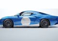 A blue Zagato AGTZ Twin-Tail #2 sports car with a large white circle on the door and red, yellow, and blue stripes on the rear side is shown in profile against a plain background, joining Christian Von Koenigsegg's car collection.