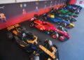A lineup of life-size F1 cars, each drivable and meticulously built from LEGO bricks, showcases official team liveries indoors against a striking branded wall.