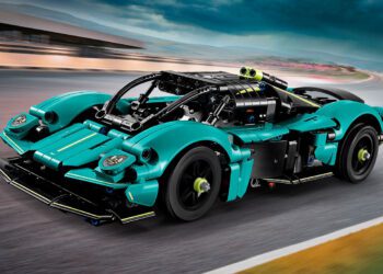 A teal and black LEGO Technic toy race car model with detailed mechanical features, inspired by the Aston Martin Valkyrie, drives on a blurred racetrack under a cloudy sky—perfect for fans looking to buy an exciting collectible.