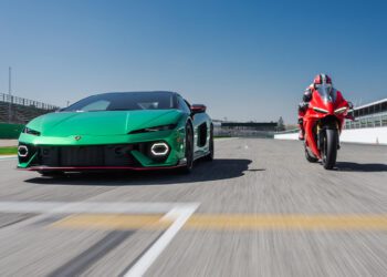 A green Lamborghini Temerario and a red Ducati Panigale V4 drive head-to-head on a racetrack under a clear blue sky.