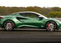 A limited edition Lotus Emira Jim Clark Edition sports car with red brake calipers is parked on asphalt, set against a backdrop of trees and a metal barrier.