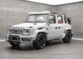 A white Mansory-modified G-Class SUV with custom bodywork and large black wheels is displayed in a modern showroom, blending luxury with bold design inspired by the Speranza G-Class Convertible.