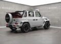 A white Mansory G-Class convertible with black wheels and a striking red leather interior is showcased in a modern showroom.