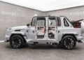 A white Mansory luxury SUV, inspired by the G-Class, showcases its open doors in a showroom adorned with "MANSORY" branding.