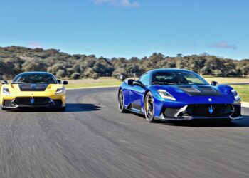 Two Maserati MC20 sports cars, one yellow and one blue, race side by side on a track with trees and blue sky in the background—hinting at how Maserati will take the spotlight at 2025 FuoriConcorso with GT2 Stradale and MCXtrema.