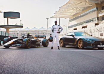 A person in a racing suit stands between a Formula 1 car and a limited-run Mercedes-AMG GT 63 on a racetrack with grandstands in the background, evoking scenes from the upcoming Brad Pitt F1 film.