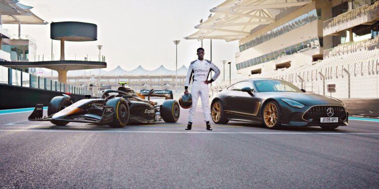 A person in a racing suit stands between a Formula 1 car and a limited-run Mercedes-AMG GT 63 on a racetrack with grandstands in the background, evoking scenes from the upcoming Brad Pitt F1 film.