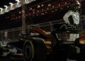 A Formula 1 driver in a racing suit and helmet stands next to his car on a lit racetrack at night, with grandstands in the background—echoing scenes from the Brad Pitt F1 film featuring the limited-run Mercedes-AMG GT 63.