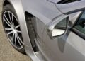 Close-up of a silver sports car—the only Mercedes-AMG Black Series to feature a V12—showing the front left wheel, side mirror, and a carbon fiber side vent on a paved surface.