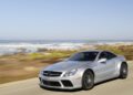 A silver Mercedes-Benz sports car, the only Mercedes-AMG Black Series to feature a V12, drives along a coastal road with the ocean and waves visible in the background.