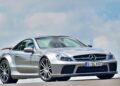 A silver Mercedes-Benz sports car, the only Mercedes-AMG Black Series to feature a V12, is parked on a road with a blue sky and clouds in the background.