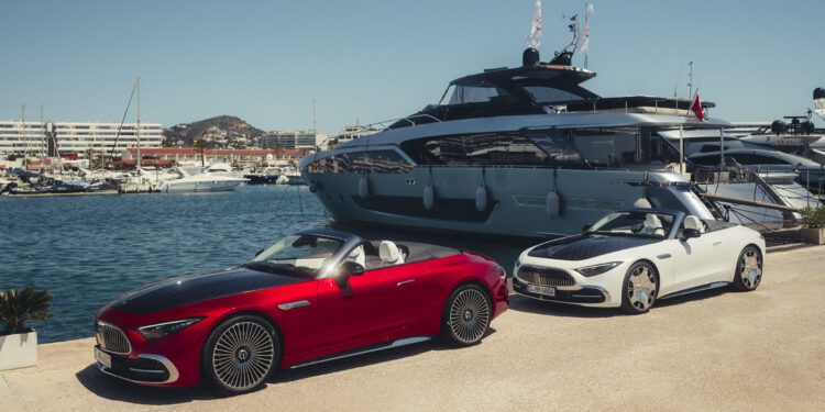 Two modern convertibles, including a striking Mercedes-Maybach SL 680, are parked on a marina dock before a luxury yacht, with other boats and waterfront buildings in the background. The 2026 Mercedes-Maybach will soon be available at select US dealers.