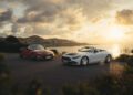 Two convertible sports cars, including a striking 2026 Mercedes-Maybach SL 680, are parked on a coastal road at sunset with a scenic view of the sea and hills in the background.