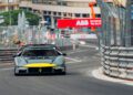 A Maserati race car drives on a city street circuit with safety barriers and signage visible in the background.