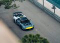 A grey and yellow Maserati supercar with a large rear wing is parked on a paved road beside a metal barrier, near some greenery—capturing the thrilling spirit of the Monaco E-Prix.
