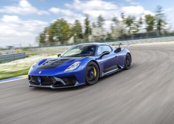 A blue Maserati GT2 Stradale speeds around a racetrack on a clear day, with trees and a blue sky in the background, capturing the thrill of the Maserati Driving Experience.
