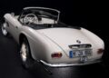A white classic BMW convertible is shown from the rear, top down, with a German license plate "M JX 800"—a striking example of how this BMW went from bold gamble to blue-chip classic.