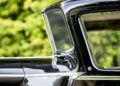 Close-up side view of a classic black Rolls-Royce Phantom with chrome trim, focusing on the roof and door against blurred green foliage—a design admired by celebrity owners for over 100 years.