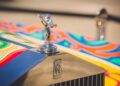 Close-up of a Rolls-Royce Phantom hood ornament and badge on a car with a colorful, psychedelic paint design, reminiscent of styles favored by celebrity owners.
