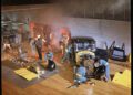 Several people in a workshop assemble and repair car parts around a vintage black Rolls-Royce Phantom; tools, equipment, and car pieces are scattered across the wooden floor.