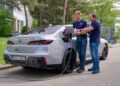 Two men stand by a silver BMW i7 electric car, with one charging the vehicle at a public station while the other checks a tablet—highlighting the future of all-solid-state EV batteries.