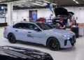 A person works on a laptop next to a BMW i7 with "Solid Power" branding in a bright, modern automotive workshop focused on all-solid-state EV batteries.